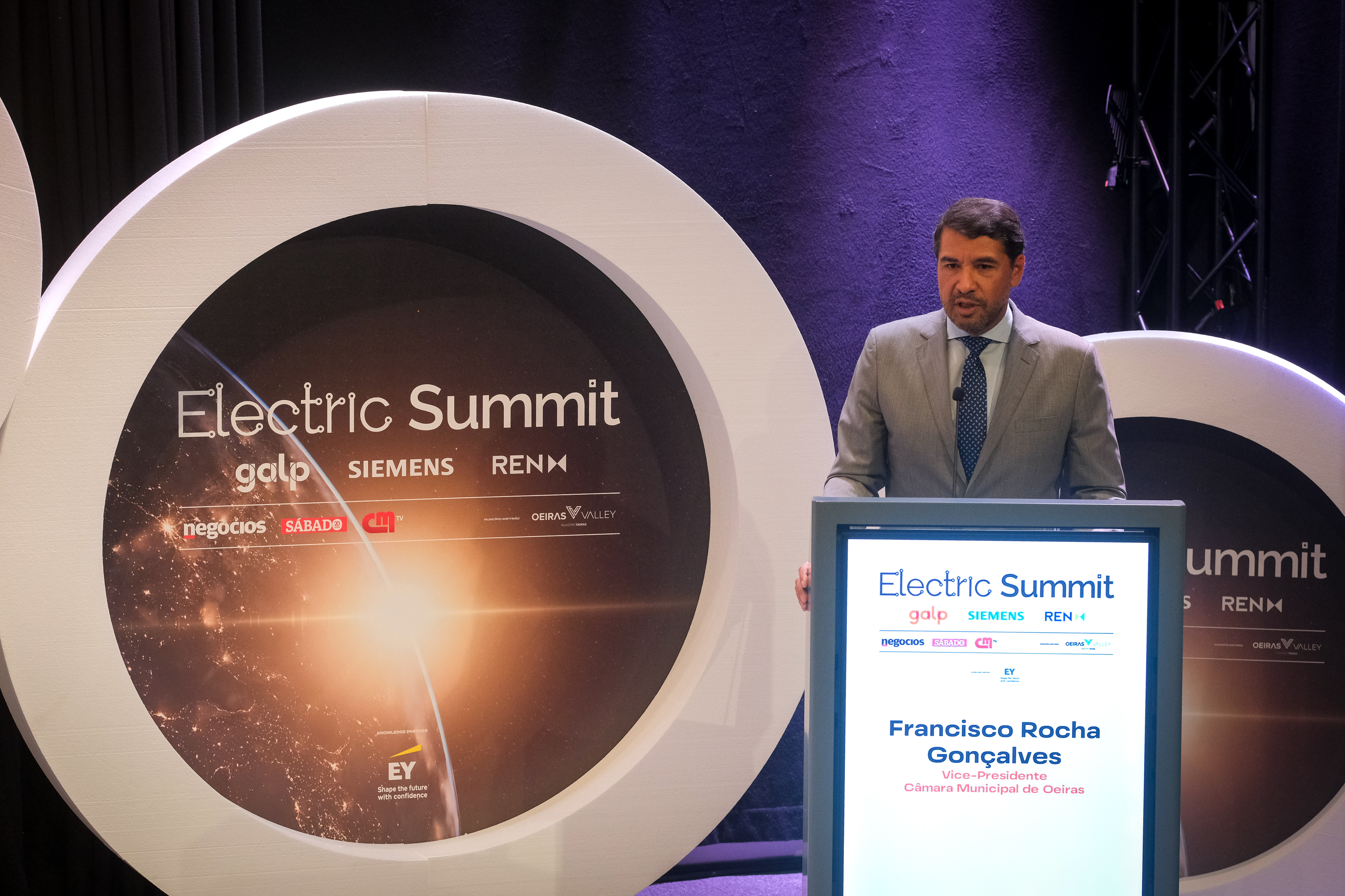 Imagem do Vice-Presidente da Câmara Municipal de Oeiras no palco do Auditório do Taguspark, no plano de fundo vê-se o cartaz do Electric Summit