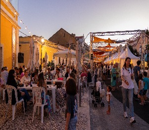 Fotografia da de várias pessoas, umas sentadas, outras a passear-se pelo evento. 