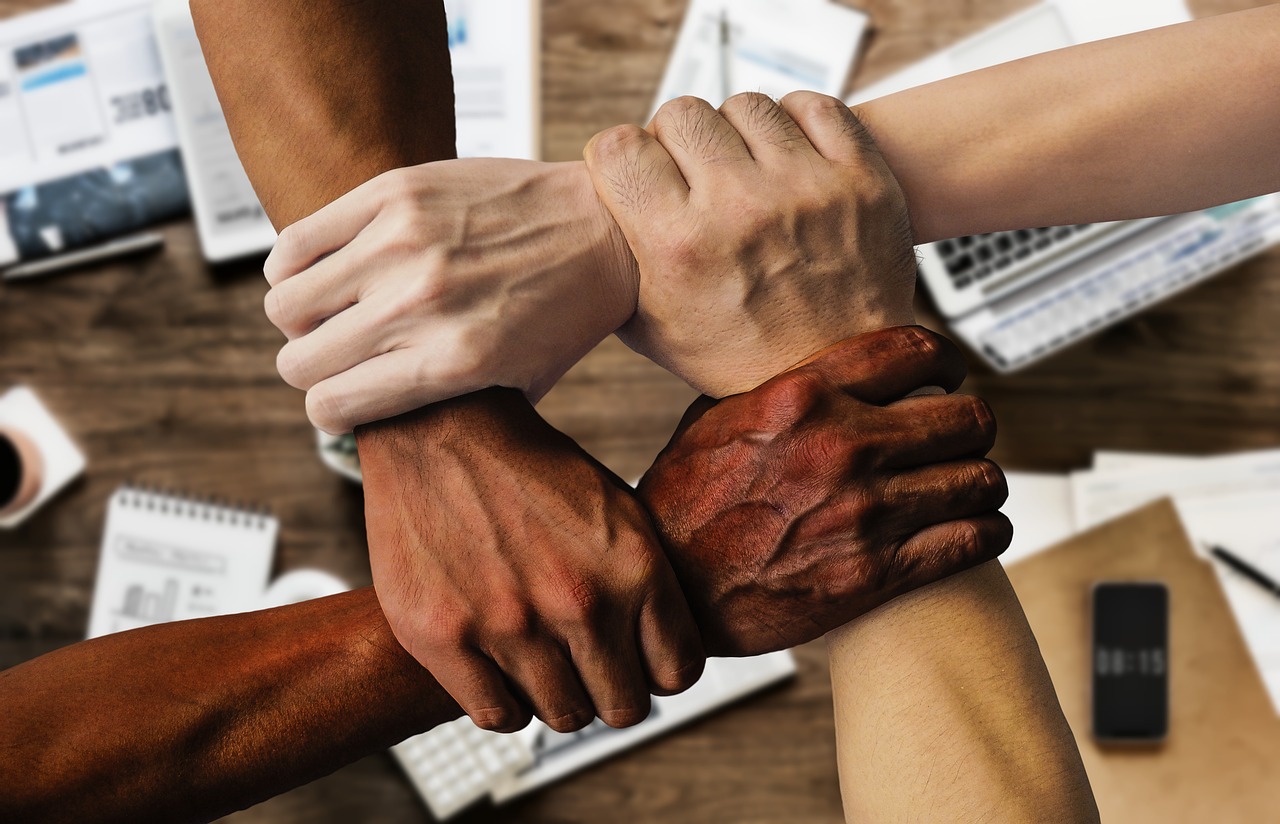 quatro mãos entrelaçadas num cenário empresarial